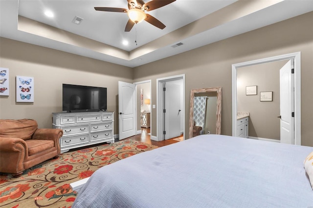 bedroom featuring a raised ceiling, ensuite bath, and ceiling fan