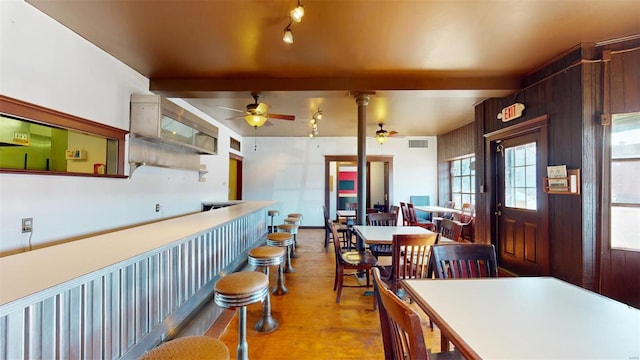 kitchen featuring ceiling fan, beamed ceiling, light hardwood / wood-style flooring, wooden walls, and ornate columns