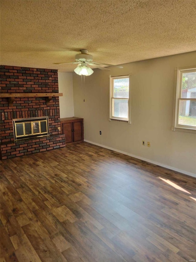 unfurnished living room with a brick fireplace, ceiling fan, a healthy amount of sunlight, and dark hardwood / wood-style flooring