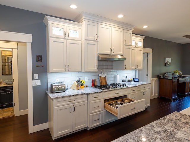 kitchen featuring white cabinets, tasteful backsplash, light stone countertops, stainless steel gas stovetop, and dark wood-type flooring