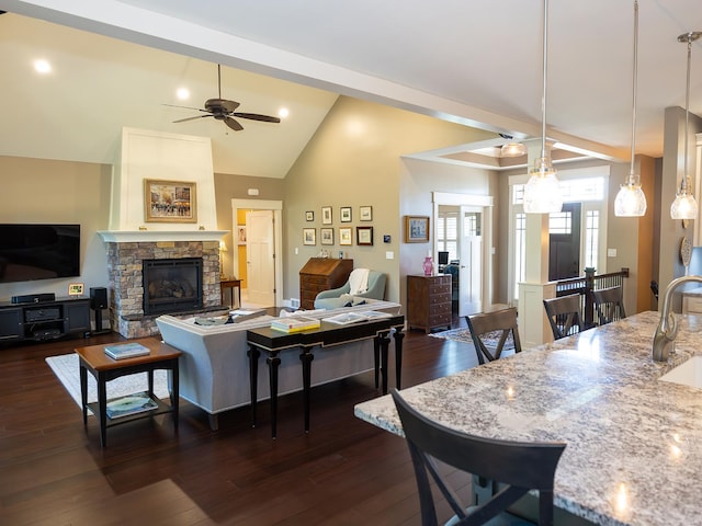 living room with ceiling fan, high vaulted ceiling, dark wood-type flooring, a fireplace, and sink