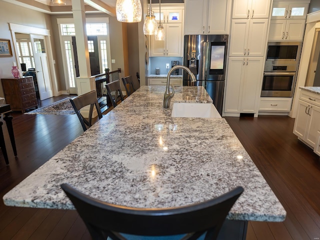 kitchen with a large island with sink, dark wood-type flooring, hanging light fixtures, stainless steel appliances, and sink