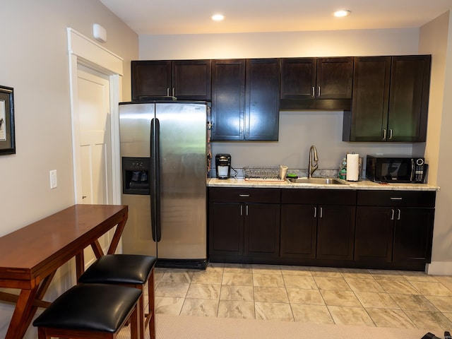 kitchen with stainless steel refrigerator with ice dispenser, dark brown cabinetry, sink, and light stone counters