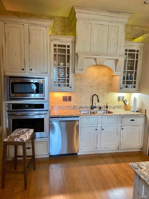 kitchen featuring light wood-type flooring, sink, backsplash, stainless steel appliances, and light stone countertops