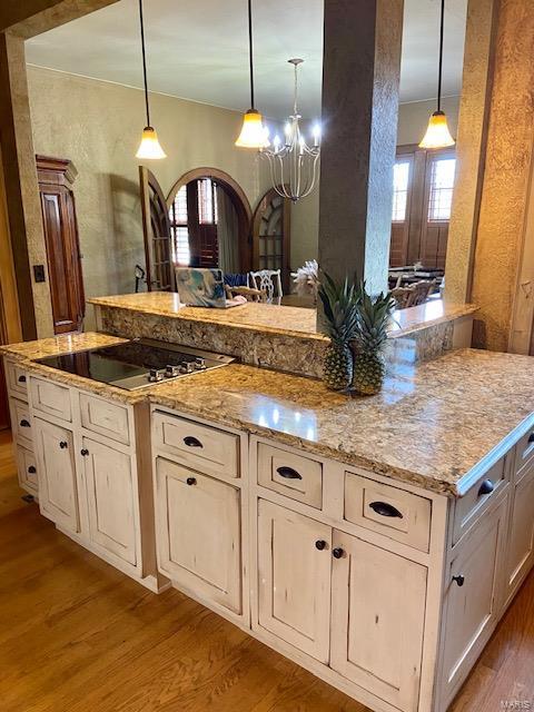 kitchen with pendant lighting, a chandelier, black electric cooktop, light stone countertops, and light hardwood / wood-style floors