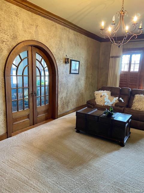 carpeted living room with an inviting chandelier, french doors, and crown molding