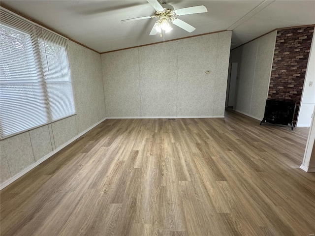 spare room featuring ceiling fan, a brick fireplace, wood-type flooring, vaulted ceiling, and ornamental molding