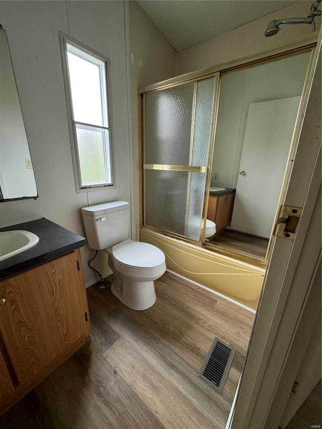 full bathroom featuring hardwood / wood-style floors, vanity, toilet, and enclosed tub / shower combo