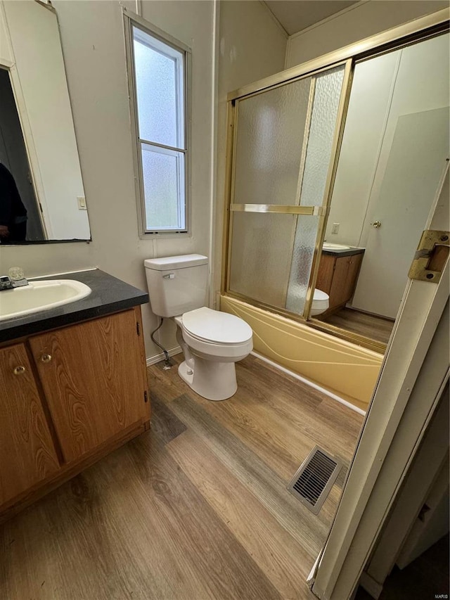 full bathroom featuring hardwood / wood-style flooring, vanity, toilet, and bath / shower combo with glass door