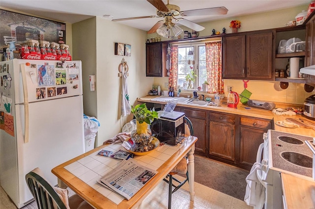 kitchen featuring ceiling fan, dark brown cabinetry, sink, and white appliances