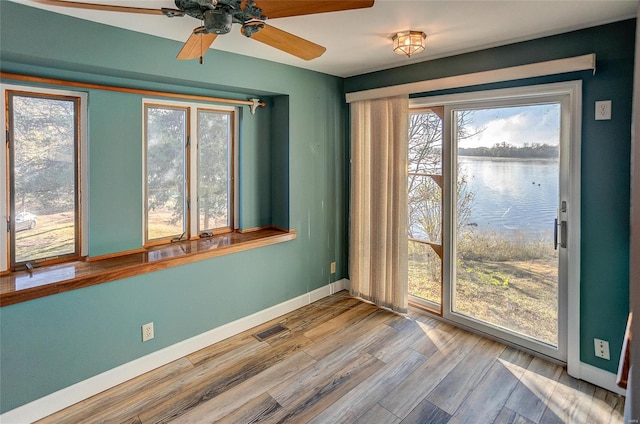 empty room featuring a wealth of natural light, a water view, hardwood / wood-style flooring, and ceiling fan