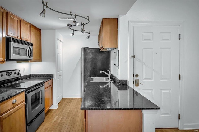 kitchen with sink, light hardwood / wood-style flooring, stainless steel appliances, and dark stone counters