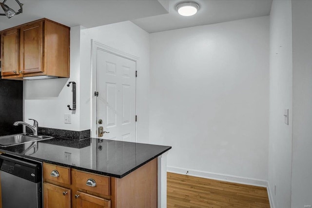 kitchen featuring stainless steel dishwasher, dark stone counters, sink, and wood-type flooring