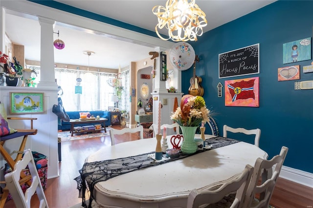 dining space featuring wood-type flooring, a notable chandelier, and decorative columns