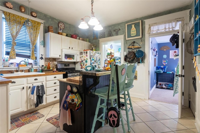 kitchen featuring hanging light fixtures, sink, light tile patterned floors, white appliances, and white cabinetry