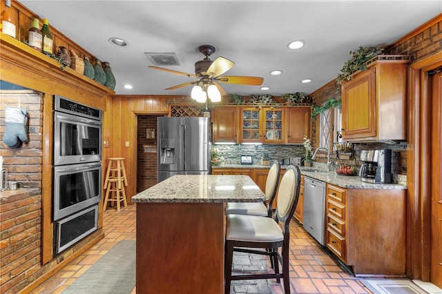 kitchen with appliances with stainless steel finishes, a breakfast bar, a kitchen island, light stone countertops, and ceiling fan