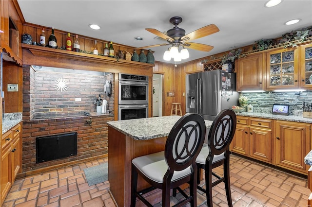 kitchen with appliances with stainless steel finishes, backsplash, ceiling fan, and light stone counters