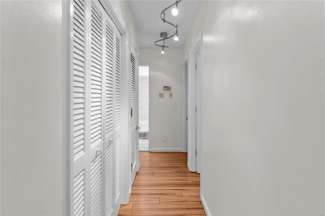 corridor with rail lighting and light hardwood / wood-style floors