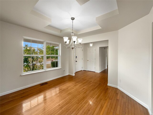 empty room with a chandelier, a tray ceiling, and hardwood / wood-style flooring