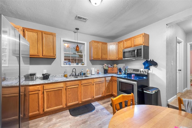 kitchen with sink, hanging light fixtures, light hardwood / wood-style flooring, a textured ceiling, and appliances with stainless steel finishes