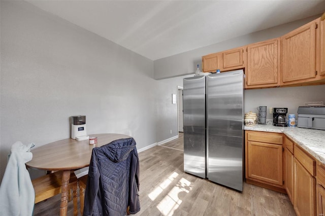 kitchen with baseboards, light brown cabinetry, freestanding refrigerator, and light wood-style floors