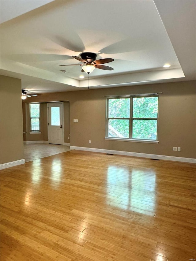 unfurnished room with a healthy amount of sunlight, a tray ceiling, ceiling fan, and light hardwood / wood-style flooring