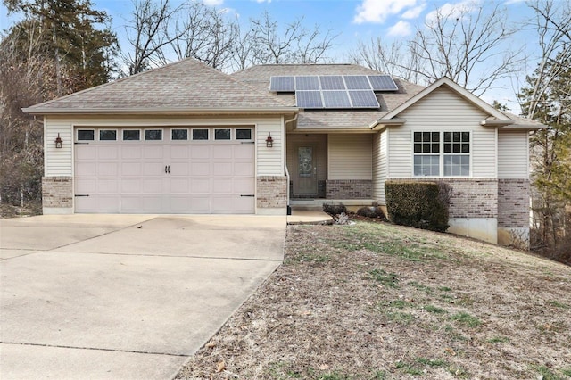 view of front of property featuring a garage, driveway, a shingled roof, roof mounted solar panels, and brick siding