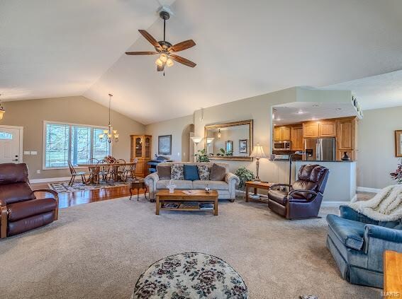 carpeted living room with ceiling fan with notable chandelier and vaulted ceiling