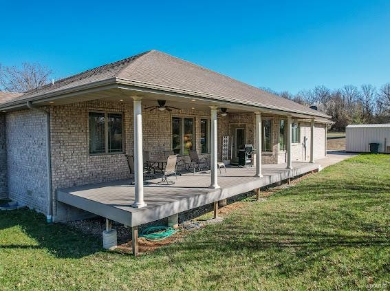 back of property with a wooden deck, ceiling fan, and a yard