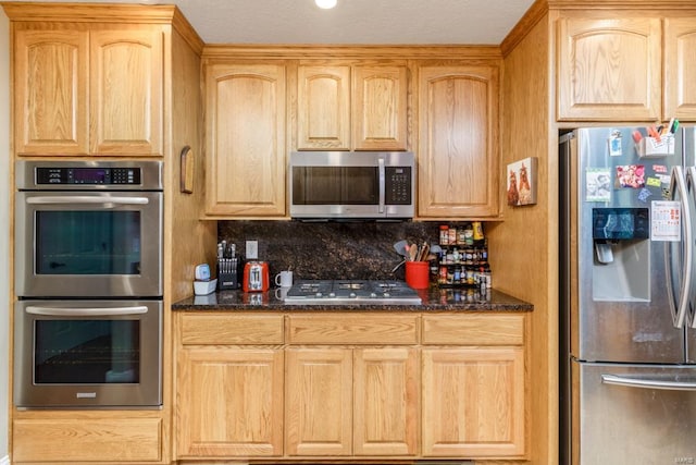 kitchen with appliances with stainless steel finishes, backsplash, dark stone countertops, and light brown cabinetry