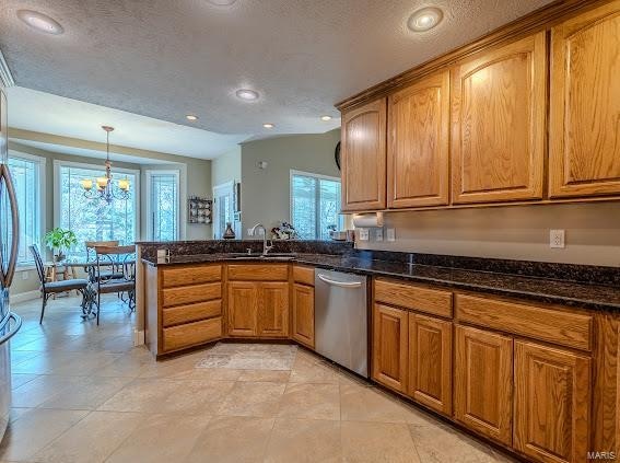 kitchen featuring dark stone counters, a chandelier, a textured ceiling, hanging light fixtures, and stainless steel dishwasher