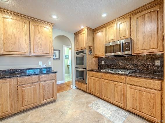 kitchen featuring appliances with stainless steel finishes, a textured ceiling, dark stone countertops, and tasteful backsplash