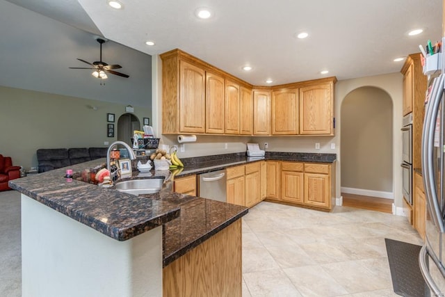 kitchen featuring appliances with stainless steel finishes, kitchen peninsula, ceiling fan, dark stone counters, and sink