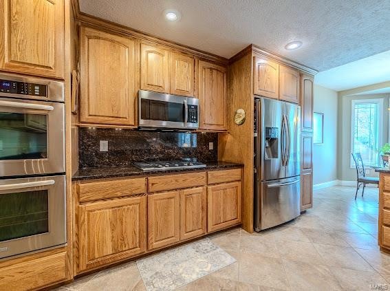 kitchen featuring light tile patterned flooring, a textured ceiling, appliances with stainless steel finishes, dark stone countertops, and decorative backsplash