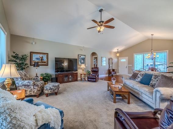 carpeted living room with ceiling fan with notable chandelier and vaulted ceiling