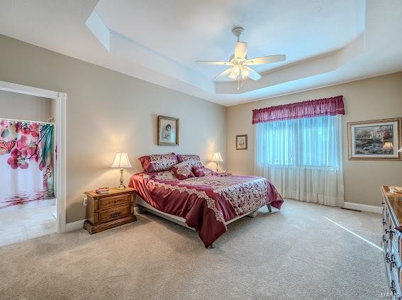 bedroom with ceiling fan, light colored carpet, a raised ceiling, and a closet