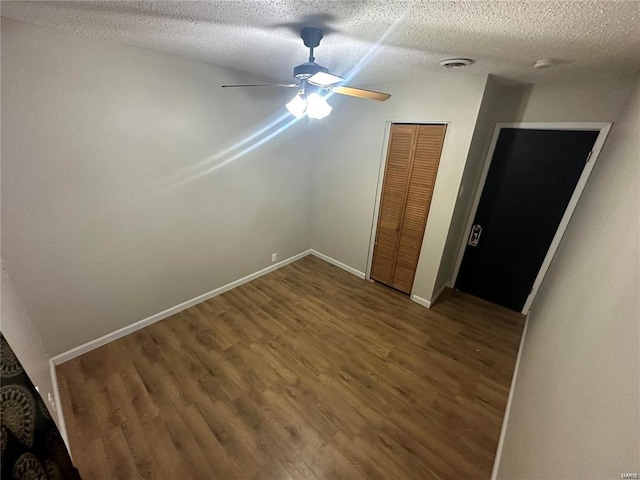 unfurnished bedroom featuring a textured ceiling, dark hardwood / wood-style flooring, ceiling fan, and a closet