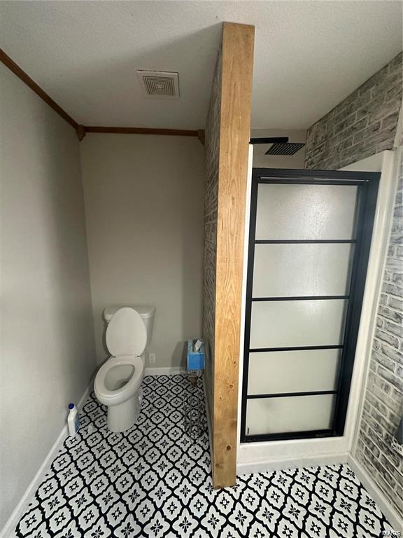 bathroom with brick wall, crown molding, a shower with shower door, and toilet