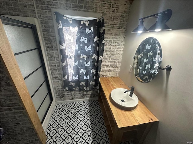 bathroom featuring walk in shower, vanity, and brick wall