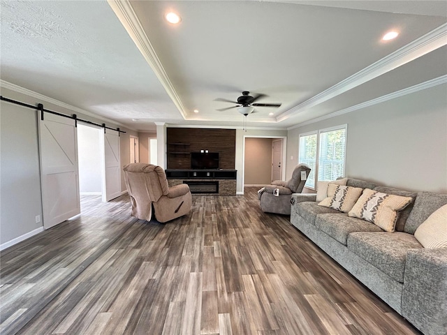 living room featuring ceiling fan, wood-type flooring, a tray ceiling, crown molding, and a barn door