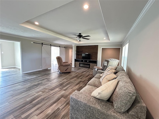 living room with ceiling fan, a tray ceiling, a barn door, crown molding, and hardwood / wood-style floors