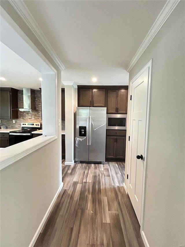 kitchen with wall chimney exhaust hood, stainless steel appliances, crown molding, dark brown cabinets, and dark hardwood / wood-style floors