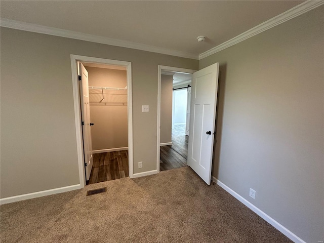 unfurnished bedroom with carpet, a closet, a walk in closet, and crown molding