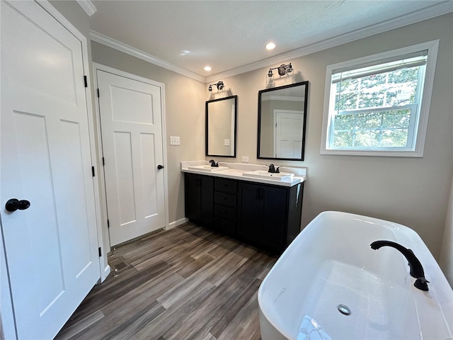 bathroom with a textured ceiling, hardwood / wood-style floors, ornamental molding, vanity, and a bathing tub