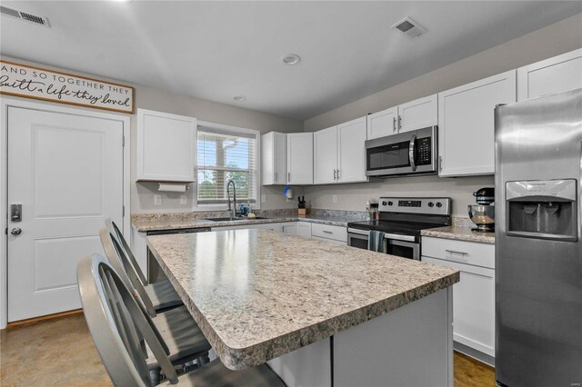 kitchen featuring sink, white cabinets, a kitchen bar, a kitchen island, and appliances with stainless steel finishes