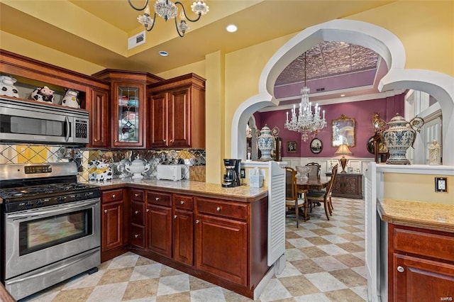 kitchen featuring decorative backsplash, light stone counters, pendant lighting, stainless steel appliances, and a notable chandelier