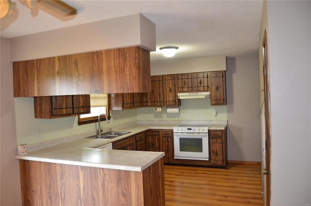 kitchen with light wood-type flooring, a textured ceiling, sink, kitchen peninsula, and oven