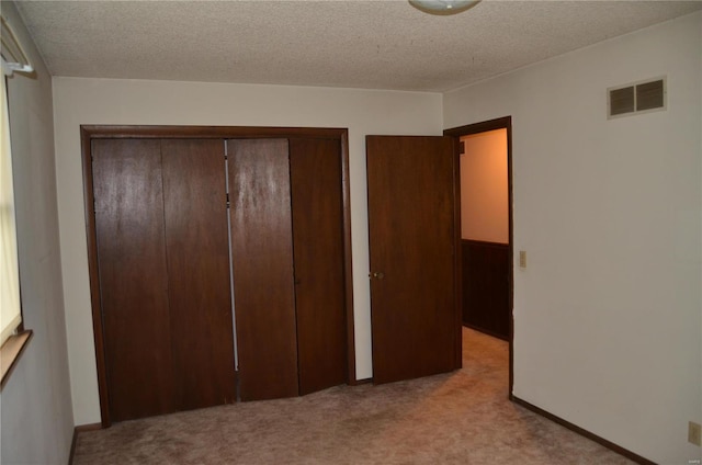 unfurnished bedroom with a textured ceiling, light colored carpet, and a closet