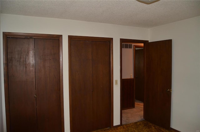 unfurnished bedroom with multiple closets, a textured ceiling, and carpet floors