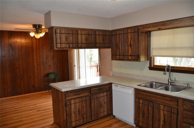 kitchen featuring white dishwasher, wood walls, sink, kitchen peninsula, and light hardwood / wood-style flooring